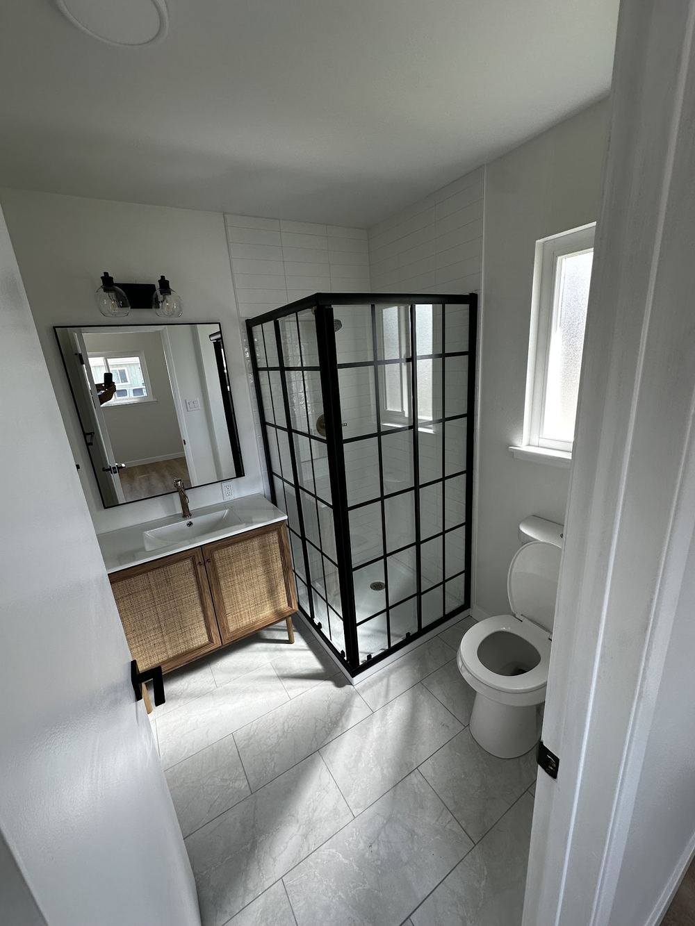 A finished bathroom with a black-framed glass shower screen, a timber vanity and large-format floor tile.