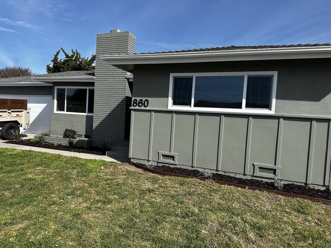 A single-storey house with fresh grey-green siding, white trim and a clean lawn.