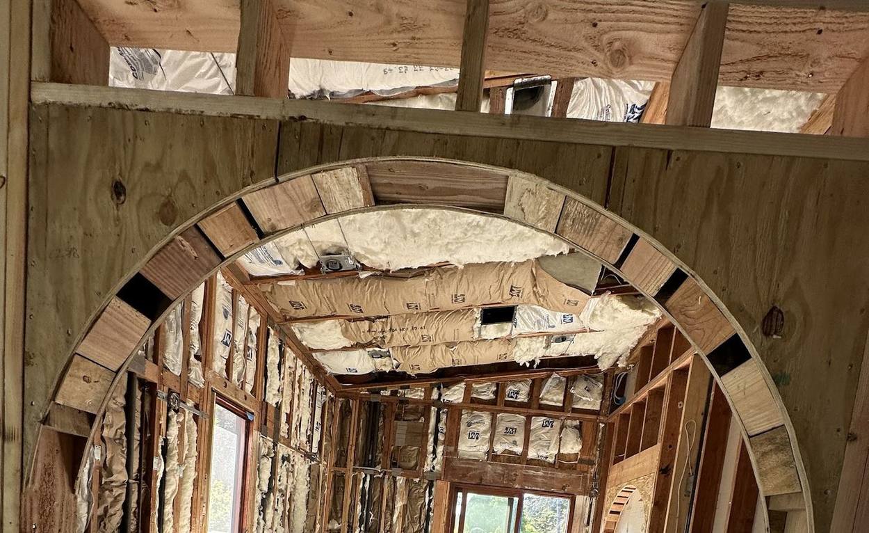 A segmented timber arch built into stud framing, with insulation batts and exposed rafters around it.