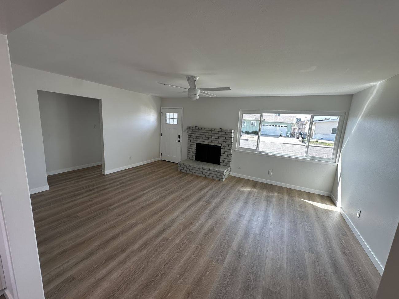 A finished living room with wood-look flooring, a brick fireplace, fresh white walls and a ceiling fan.